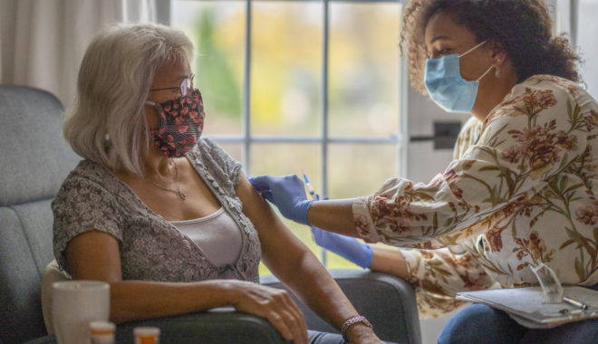 Senior woman getting a vaccine from her doctor in her home during a house visit during the COVID-19 pandemic