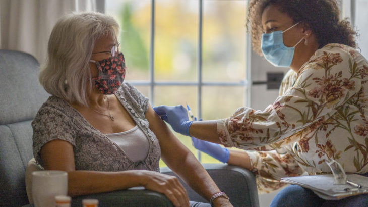 Senior woman getting a vaccine from her doctor in her home during a house visit during the COVID-19 pandemic